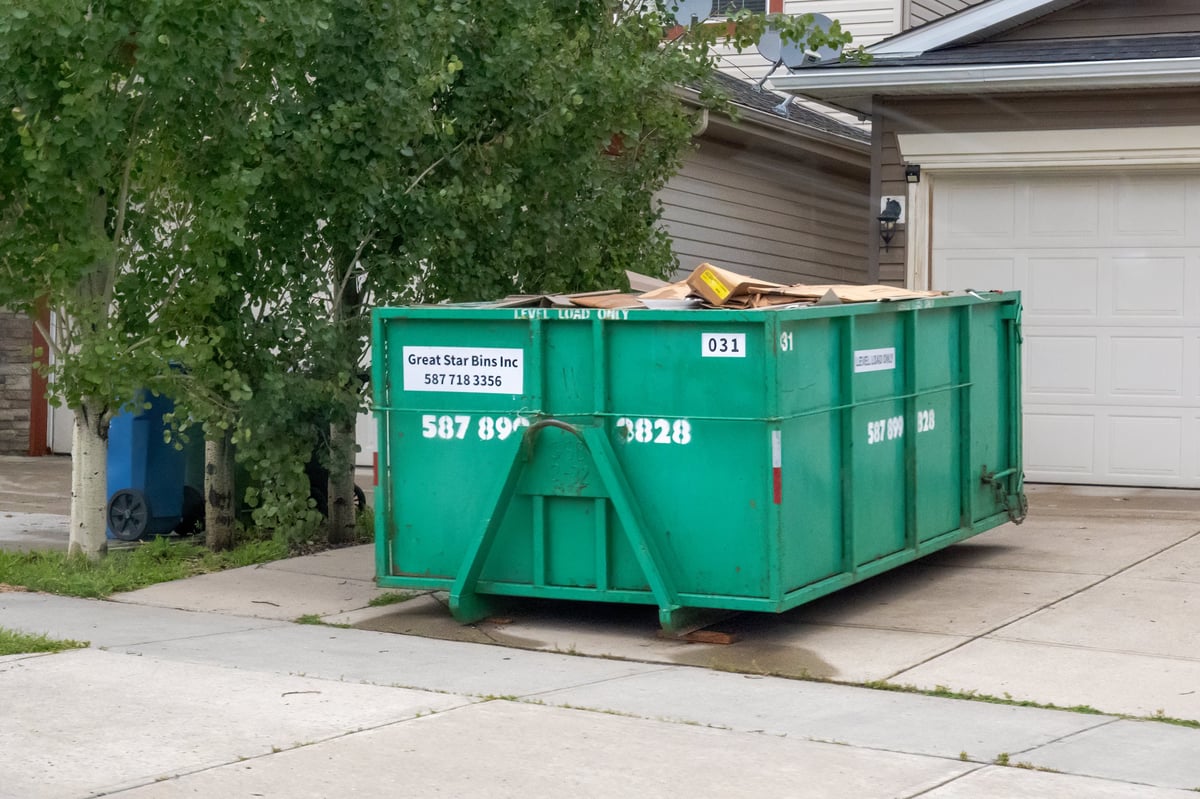 A green roll-off dumpster filled with debris parked in a residential driveway