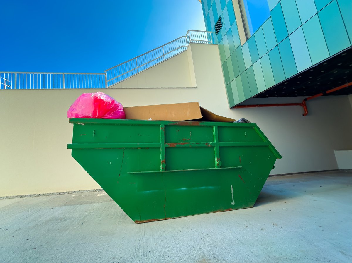 A green dumpster filled with trash bags and cardboard